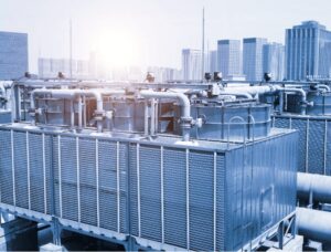 Commercial rooftop cooling tower system used in HVAC operations for industrial buildings, showing condenser units, heat exchangers, and piping under bright daylight.