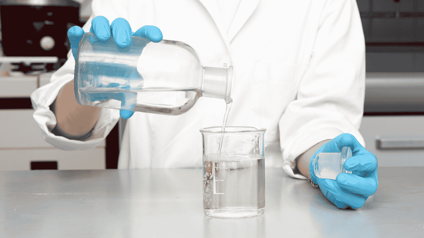 A laboratory technician pours a water sample into a beaker for measuring alkalinity, total alkalinity, p alkalinity, hydroxide alkalinity, water chemistry, and pH analysis to determine alkalinity levels and buffering capacity.